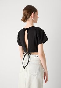 Fekete crop top rövid ujjal és hátsó megkötéssel. Világoskék farmer szoknyával viselve, amely címkével és hátsó zsebekkel rendelkezik.