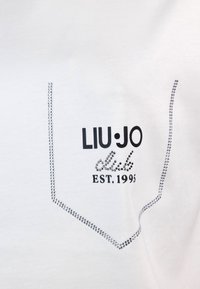 T-shirt bianca a maniche corte con design della tasca decorato con strass argentati. Il testo stampato in nero recita “LIU·JO club EST. 1995.”