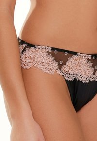 Zwarte string met doorzichtige stof, versierd met ingewikkelde roze kantdetails bij de tailleband, met florale patronen en geschulpte randen.