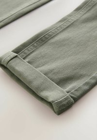 Olivza zaļa denima bikses ar salocītu maliņu, ar teksturētu audumu un smalku diagonālu aušanu. Vienkāršs, tīrs dizains.