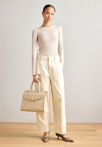 Beżowy, prążkowany top z długim rękawem w połączeniu z kremowymi spodniami o szerokich nogawkach; duża, strukturalna beżowa torebka, buty na wysokim obcasie z metalicznymi akcentami, drewniana podłoga.