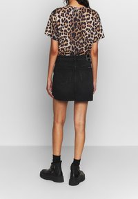 Kvinna i leopardmönstrad kortärmad topp, svart denimkort kjol, svarta strumpor och svarta kängor med spänne, står med ryggen mot kameran.