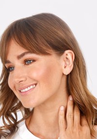 Boucles d'oreilles en or en forme de cerceau avec un design fin et circulaire, présentant une texture lisse et un minimalisme dans les ornements, portées par une femme aux cheveux ondulés.