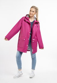 Rosa vattentät jacka med huva, stora framfickor, dragkedja och grå inredning. Bärs över en randig skjorta och jeans.