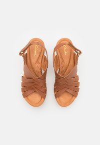 Sandales en cuir marron avec des lanières entrecroisées et une boucle à la cheville. Semelle intérieure rembourrée avec de petites perforations pour la respirabilité.