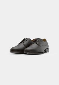 Scarpe eleganti in pelle nera con texture liscia, punta arrotondata e design con lacci. Presentano un tacco basso e piatto e dettagli di cucitura discreti.