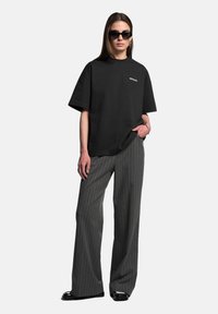 Černé oversized tričko s bílým logem, spárované s šedými proužkovanými širokými kalhotami a černými slunečními brýlemi. Jednoduchý design a uvolněný střih.