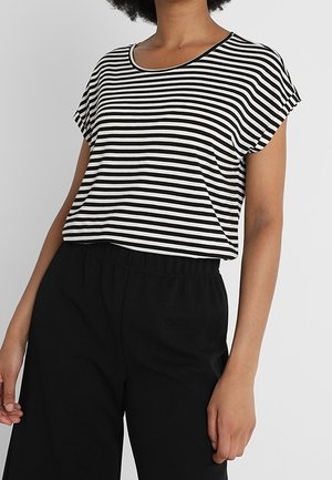 Vrouw die een zwart-wit gestreepte top met korte mouwen draagt, ingestopt in een hoge taille zwarte broek, staand tegen een effen achtergrond.