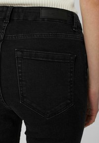 Czarne dżinsy z denimu z tylną kieszenią z charakterystycznym trójkątnym wzorem ściegów oraz prostokątną metką marki na pasku.