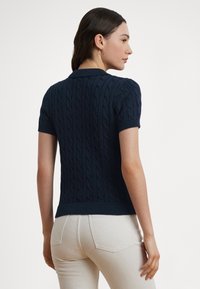 Tmavomodrý sveter krátkych rukávov s pleteným vzorom a priliehavým strihom so žebrovaným lemom. Látka má textúrovaný vzor, ktorý zdôrazňuje klasický štýl.