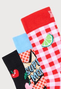 Τρεις πολύχρωμες κάλτσες με διαφορετικά σχέδια: μαύρη με κεράσια, ροδακινί με το κείμενο "Super Mom" και μπλε μανσέτα, κόκκινη καρό με λωρίδα λάιμ.