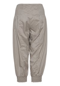 Pantalon beige clair à coupe large avec taille et poignets élastiques, détails de couture froncée, vu de dos avec une petite étiquette de marque sur la taille.