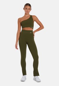 Olijfgroene geribbelde crop top met een enkel schouderontwerp, gecombineerd met bijpassende high-waisted leggings. Beide hebben subtiele logoaccenten.