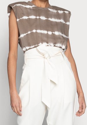 Bezrekawikowy top taupe w stylu tie-dye, zestawiony z białymi spodniami z wysokim stanem, posiadającymi szeroki pasek zawiązany na kokardę w talii.