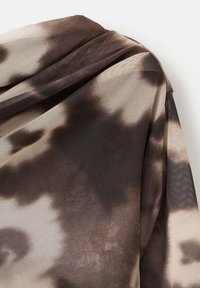 Material textil cu un model maro și bej, având o textură similară cu plasă, cu pliuri moi și un design lejer. Remarcabil prin variațiile sale subtile de culoare.