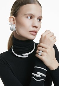 Conjunto de joyería de plata que incluye un collar grueso, pendientes, anillos y pulseras, todos adornados con brillantes rhinestones en varias formas.