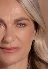 Zbliżenie na twarz z jasną skórą, gładką teksturą, jasnobrązowymi włosami z refleksami i niebieskimi oczami. Subtelny makijaż na ustach i powiekach.
