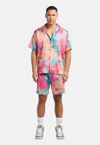 Fargerik kortermet skjorte og matchende shorts i rosa, blå og oransje mønstre. Materialet er lettvektig, med en glatt, blank overflate.