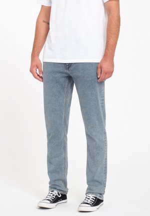 Jeans de mezclilla de color azul claro, con corte recto, diseño de cinco bolsillos y combinados con zapatillas negras y blancas.