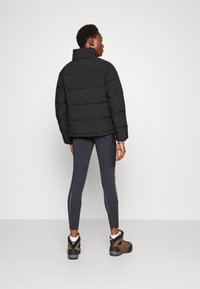 Czarna ocieplane kurtka z wysokim kołnierzem, w połączeniu z ciemnymi legginsami z jasnoniebieskimi akcentami oraz brązowymi butami trekkingowymi.