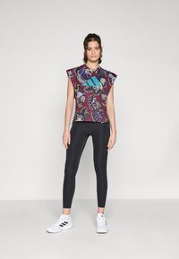 Haut sans manches multicolore avec des motifs de papillons, leggings noirs ajustés et chaussures de sport blanches avec des accents noirs.