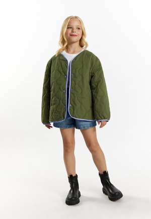 Quiltet grøn jakke med blå kanter, trykknapper, oversized pasform, båret over en hvid skjorte, parret med denim shorts og sorte støvler.