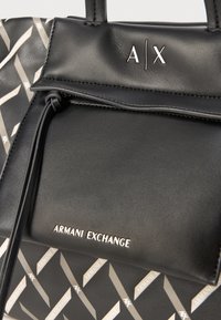 Melnas ādas rokassomas ar ģeometrisku pelēku rakstu, aprīkota ar sudraba detaļām un iegravētu "ARMANI EXCHANGE" logotipu.