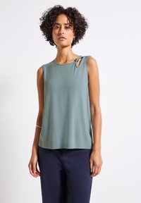 Mouwloze top in gedempt teal, met een ronde halslijn, zijsplitten en een decoratieve gesp op de schouder. Glad textuur van de stof.