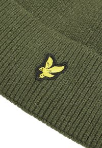 Berretto lavorato a maglia verde con una texture a costine e un logo di un uccello giallo ricamato su una toppa nera.