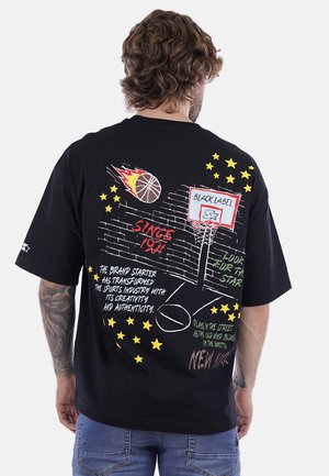 T-shirt nera oversize con grafiche colorate di un canestro da basket, fiamme, stelle e testo sul retro. Materiale in cotone, design casual.