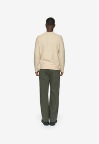 Pull en laine beige avec un col rond, associé à un pantalon vert ample. La tenue a une silhouette décontractée et est complétée par des chaussures noires.