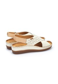Beige Leder-Sandalen mit perforiertem Design, Kreuzriemen vorne, elastischem Fersenriemen und brauner Gummisohle. Genähte Akzente entlang der Kanten.