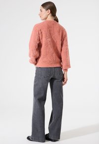 Suéter rosa de peluche con una superficie texturizada, que presenta mangas largas y cuello redondo. Combinado con jeans de pierna ancha grises de cintura alta.