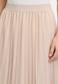 Gonna in tulle plissettata beige chiaro con vita elastica; tessuto trasparente con delicate linee verticali, che mette in mostra un design morbido e fluido.