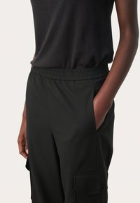 Zwarte elastaine broek met een elastische taille, zijzakken en details in cargostijl, gemaakt van zachte stof. Geschikt voor een comfortabele of casual uitstraling.