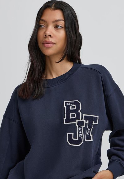 Námornícka modrá mikina vyrobená z bavlny, s okrúhlym výstrihom, spustenými ramenami a vyšitými bielymi a tmavomodrými písmenami vpredu.