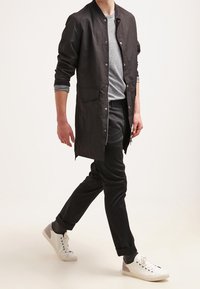 Svart lättviktsjacka, grå randig skjorta, svarta byxor och vita sneakers med grå accenter. Rakt snitt och avslappnad design.
