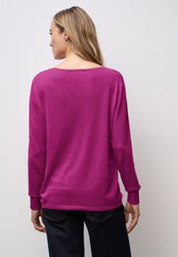 Fuchsia Langarmpullover mit weitem Halsausschnitt, gerippten Bündchen und Saum. Glatte Textur und lockere Passform, kombiniert mit dunkler Jeans.