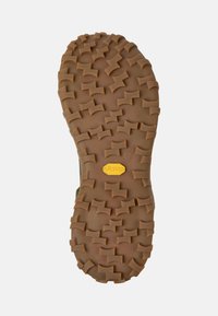 Vibram-pohja, jossa on teksturoitu, tummanruskea kumipinta, jossa on uramalli pidon lisäämiseksi ja keltainen logo keskellä.