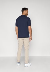 Ναυτικό κοντομάνικο πουκάμισο συνδυασμένο με μπεζ παντελόνι και λευκά αθλητικά παπούτσια. Απλός σχεδιασμός, κανονική εφαρμογή και λεία υφή.