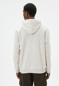 Sudadera gris de tela suave, con yugo trasero, capucha con cordón y puños y borde acanalados. Diseño simple y minimalista, sin patrones.