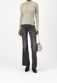 Haut à manches longues côtelé vert clair avec une coupe ajustée. Jeans évasés gris foncé avec deux poches avant. Bottines noires à talons. Sac à main beige.