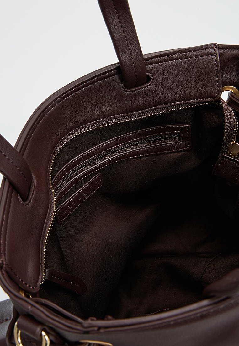 Intérieur d'un sac tote en cuir marron avec des poches zippées et des poches plaquées. Texture lisse, anses supérieures et accents en hardware doré.