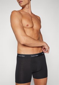Melni boksa šortai ar elastīgu jostu, kas rotāta ar "Calvin Klein" zīmolu. Mīksta auduma, pieguļošs dizains ar vidukļa garumu.