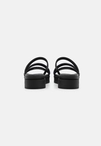 Sandales noires avec trois brides croisées, une semelle intérieure rembourrée et une semelle plateforme épaisse. La texture semble lisse et mate.