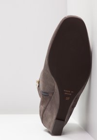 Bottine à talon en daim marron avec fermeture éclair latérale et boucle dorée, semelle marquée "Fabriqué en Espagne" et taille 37.