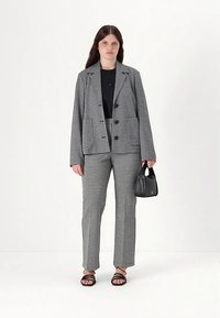 Szara i czarna marynarka w kratę z dopasowanymi spodniami. Charakteryzuje się luźnym krojem, dużymi guzikami i małą czarną torebką. Czarne sandały na otwarty palec.