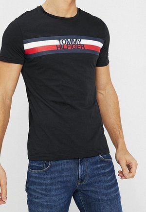 Black cotton T-shirt featuring a horizontal striped design in red, white, and blue, with "TOMMY HILFIGER" printed in the center.