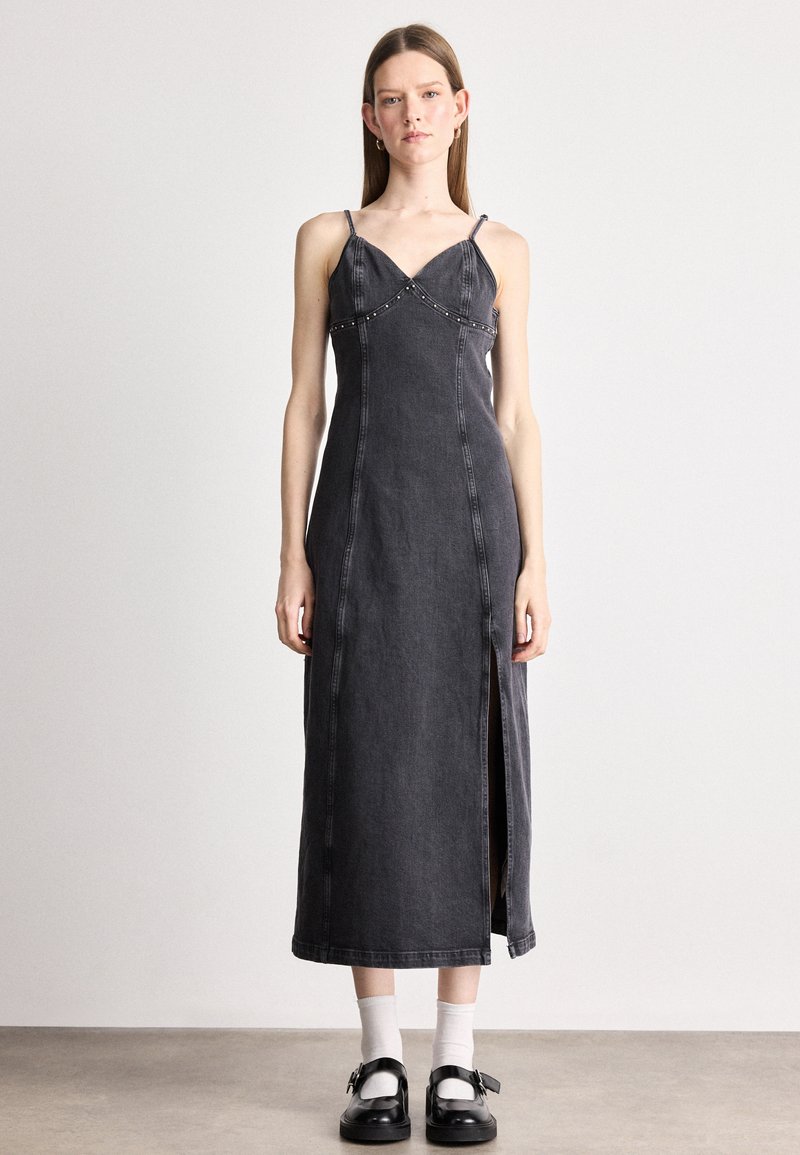 Vestido maxi de ganga preto com alças finas, decote em V, tachas decorativas ao longo do busto e uma fenda lateral para um detalhe adicional.