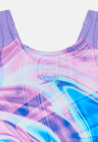 Speedo fürdőruha, amely a rózsaszín és kék hullámminták keverékét mutatja, szilárd levendula vállkialakítással és a Speedo logójával, amely visszafogott mintázatban jelenik meg.